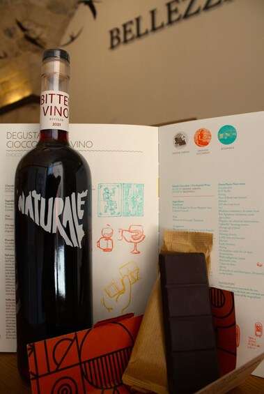 A bottle of 'NATURALE' wine with a label, a booklet with text and illustrations, and a wooden box with a red and black design. 5