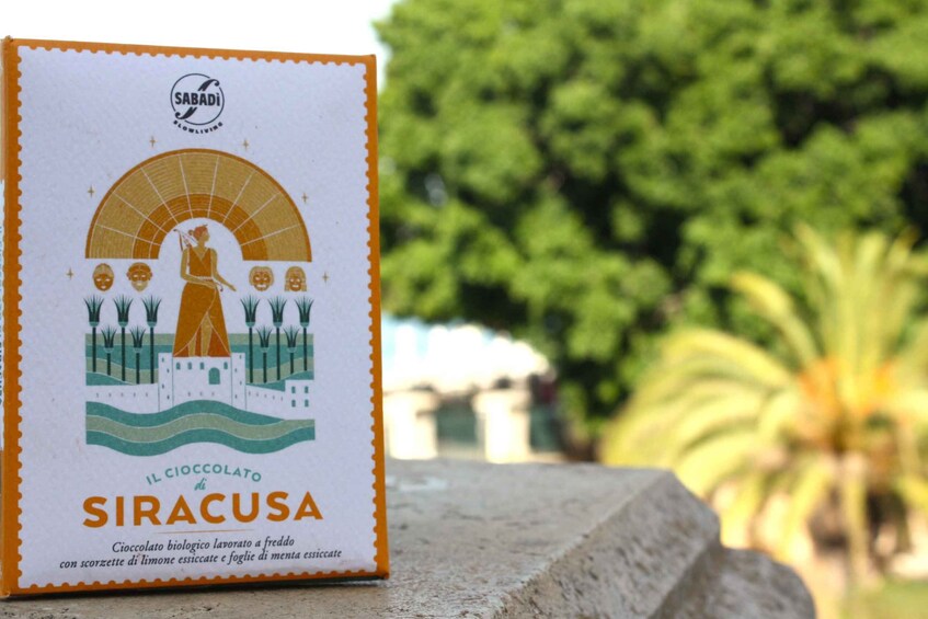 A book titled 'Il Ciocolato di Siracusa' with a cover illustration of a woman, a building, and trees. 1