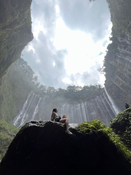 A person sitting on a rock with a waterfall in the background. 1