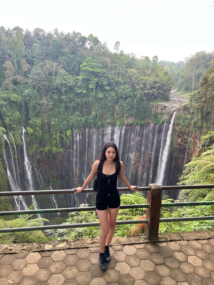 A person standing by a hexagonal-tiled walkway with a waterfall in the background. 3