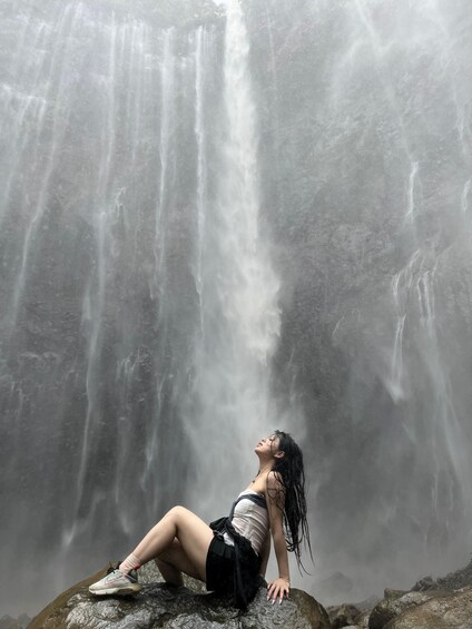 A person sitting on a rock in front of a waterfall. 5