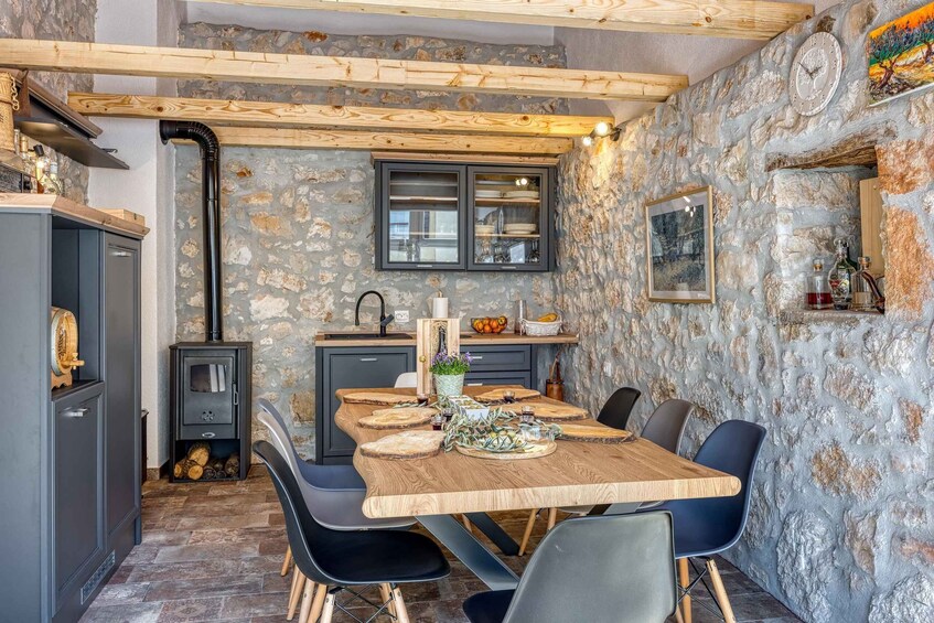 A rustic kitchen with stone walls, wooden beams, and a dining table set for six. 5