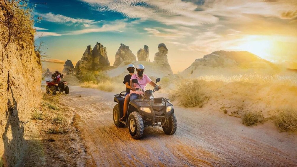 A dirt road with off-road vehicles, rocky terrain, and a sunset. 1