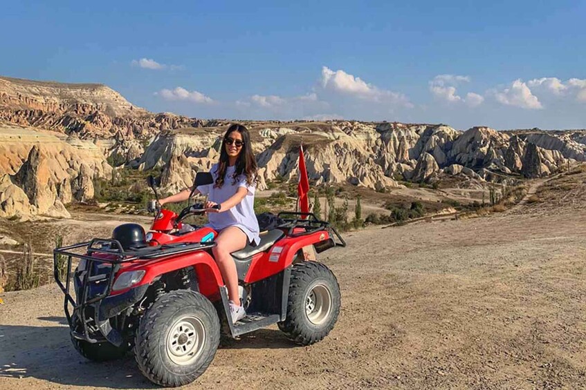 Eine Person fährt mit einem roten Quad auf einer unbefestigten Straße vor einer felsigen Landschaft. 3