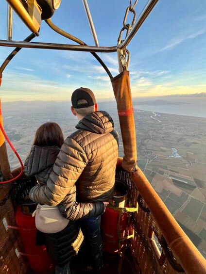 A person in a jacket and cap looking out from a gondola, with a clear view of a landscape below. 1
