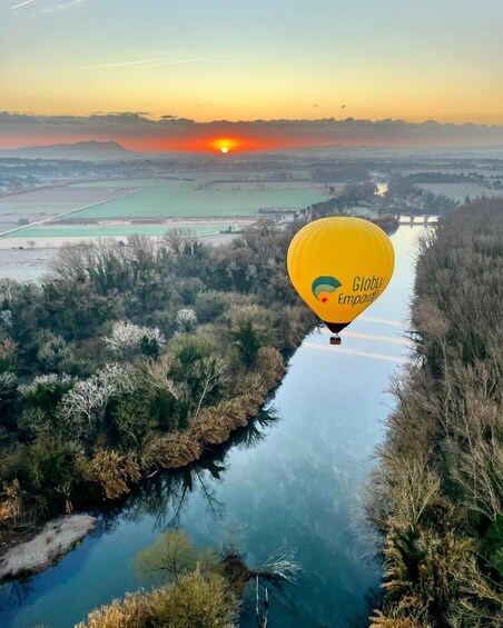 A hot air balloon over a river with fields and a sunset in the background. 2