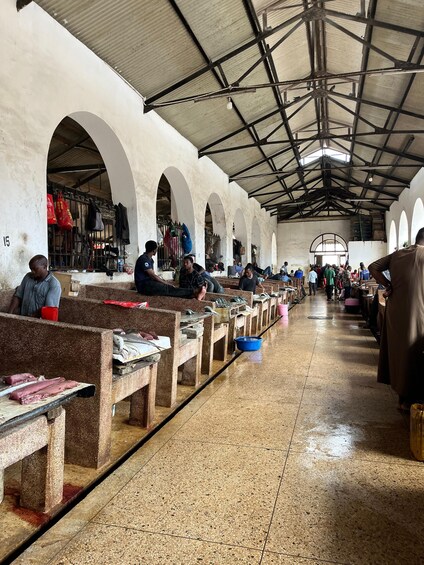 Un mercado techado con hileras de bancos y gente sentada. 3