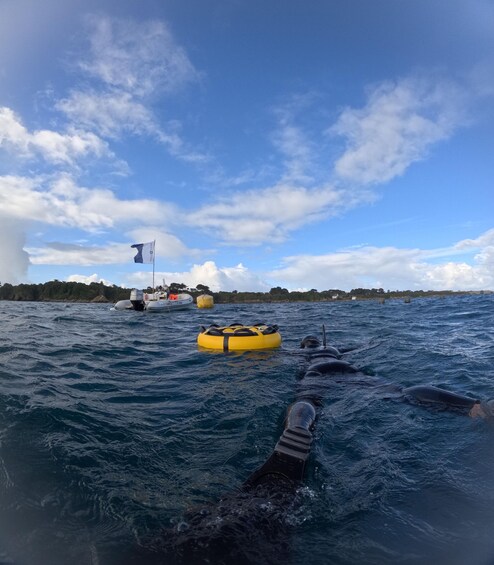 A person swimming in the ocean with a yellow flotation device and a boat in the background. 4