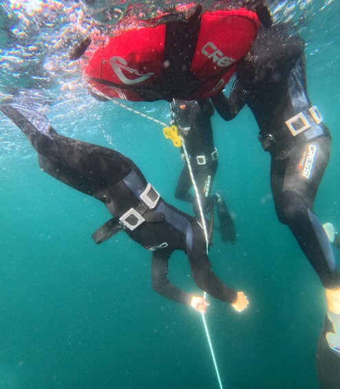 Two scuba divers underwater with red and black wetsuits, connected by a tether. 1