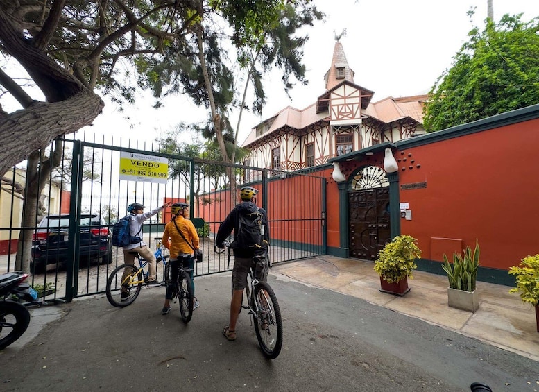 A gated entrance with a sign, a building with a tower, and cyclists. 5