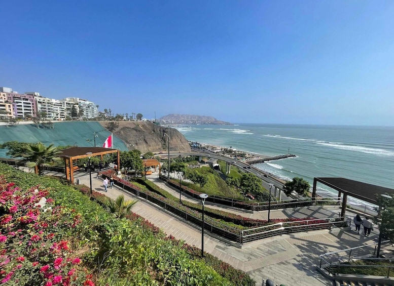 A coastal promenade with a view of the ocean, a covered pavilion, and a hillside with buildings. 4