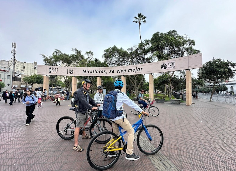A group of cyclists at a park entrance with a sign that reads 'Miraflores, se vive mejor' and 'Team Peru.' 2