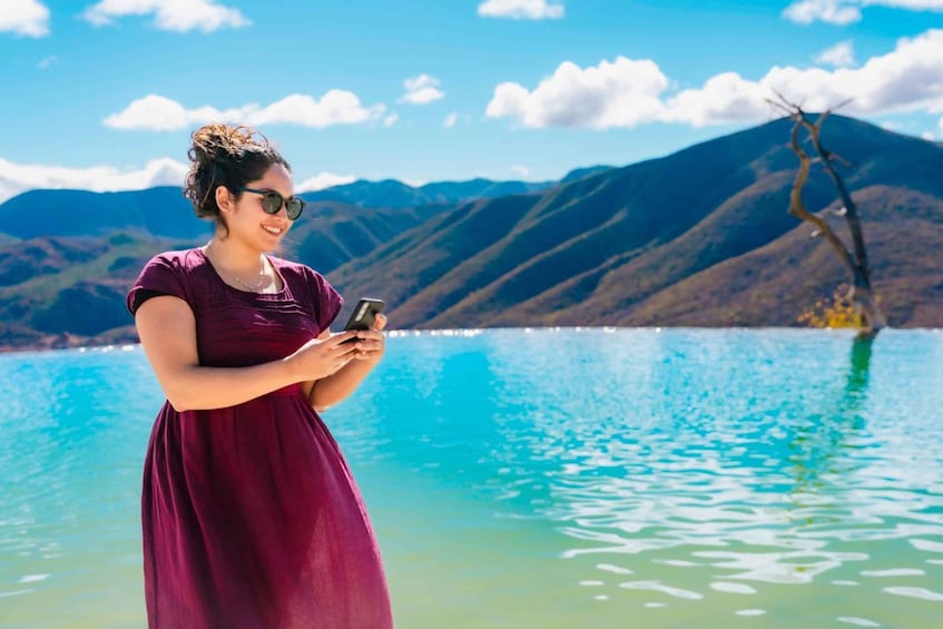 A person in a purple dress standing by a lake with mountains in the background. 1
