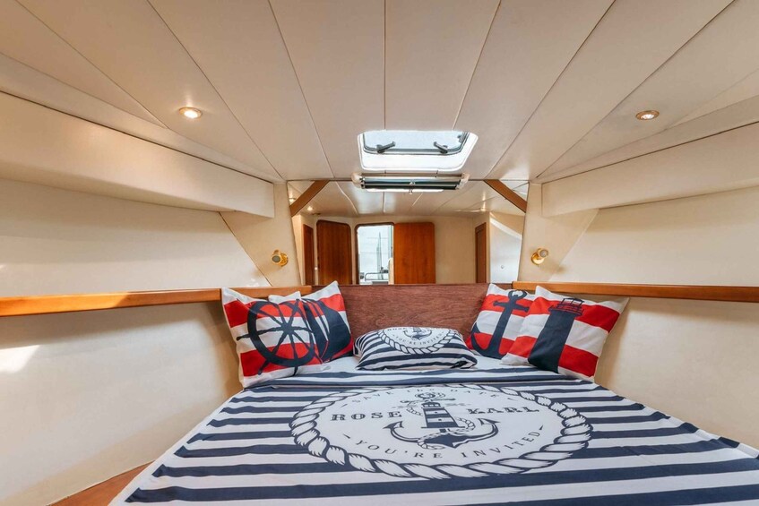 A narrow, well-lit interior with a bed featuring nautical-themed bedding and pillows. 5