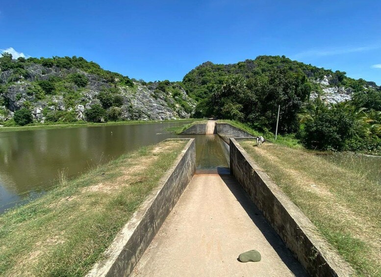 Un canal con una esclusa de hormigón, rodeado de vegetación exuberante y colinas rocosas. 5