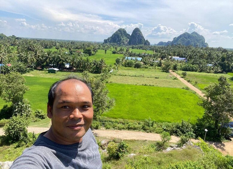 Un hombre con suéter gris tomándose un selfie con un exuberante paisaje verde y montañas al fondo. 2