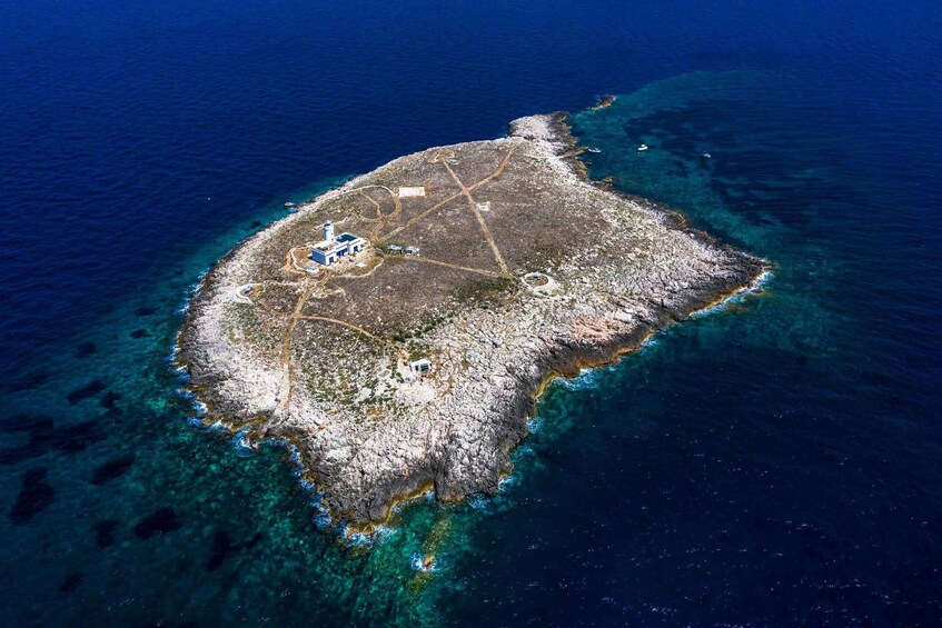 An aerial view of a small island with clear blue waters, rocky terrain, and a lighthouse. 3