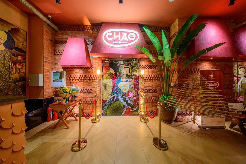 A traditional Vietnamese restaurant interior with a prominent 'CHAO' sign, decorative wall art, and a large potted plant. 3