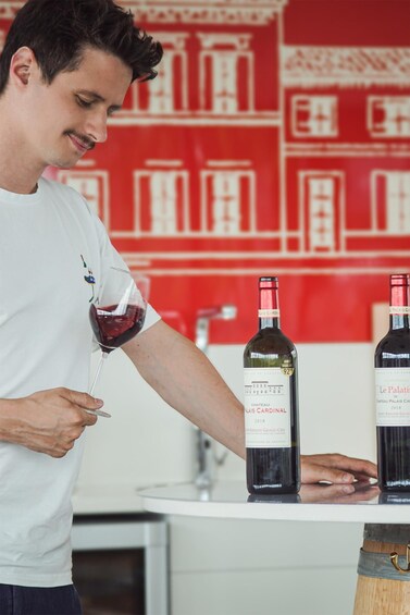 A person holding a wine glass with red wine, standing next to two bottles of Chateau Palatier 2018 wine. 5