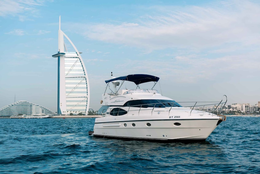 A white yacht with a blue canopy on the water, a sailboat, and the Burj Al Arab hotel in the background. 1