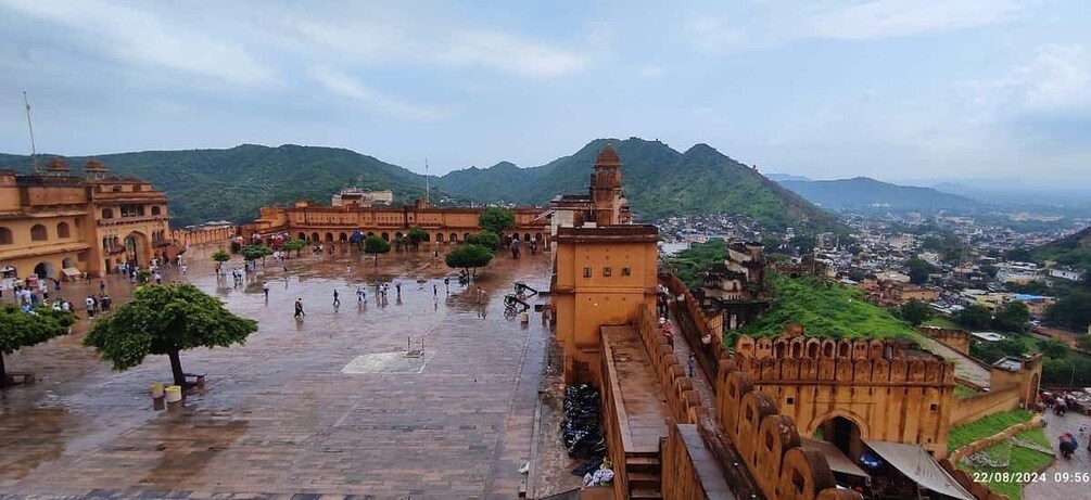 A historic fort with a large courtyard, surrounded by lush green hills and a distant cityscape. 4