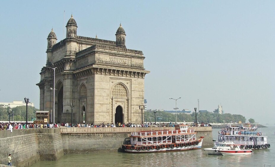 The Gateway of India with boats docked in the water and people on the bridge. 2