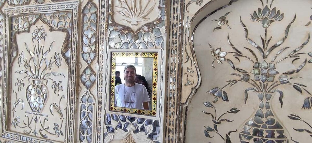 A person standing in front of a mirror with ornate floral and geometric patterns. 3