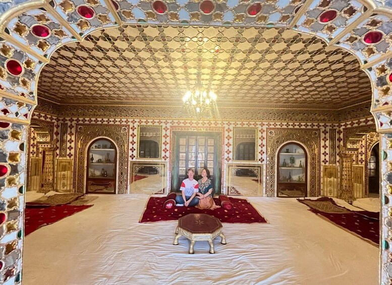 An ornate room with intricate gold and red patterns, a chandelier, and a central seating area. 5