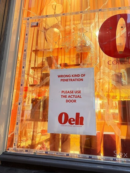 Et butiksvindue med et skilt, der står 'WRONG KIND OF PENETRATION PLEASE USE THE ACTUAL DOOR', og butikkens navn 'Oeh Concept Store Amsterdam'. 3