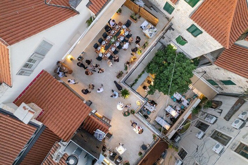 An aerial view of a courtyard with multiple seating areas, a central tree, and surrounding buildings with red-tiled roofs. 3