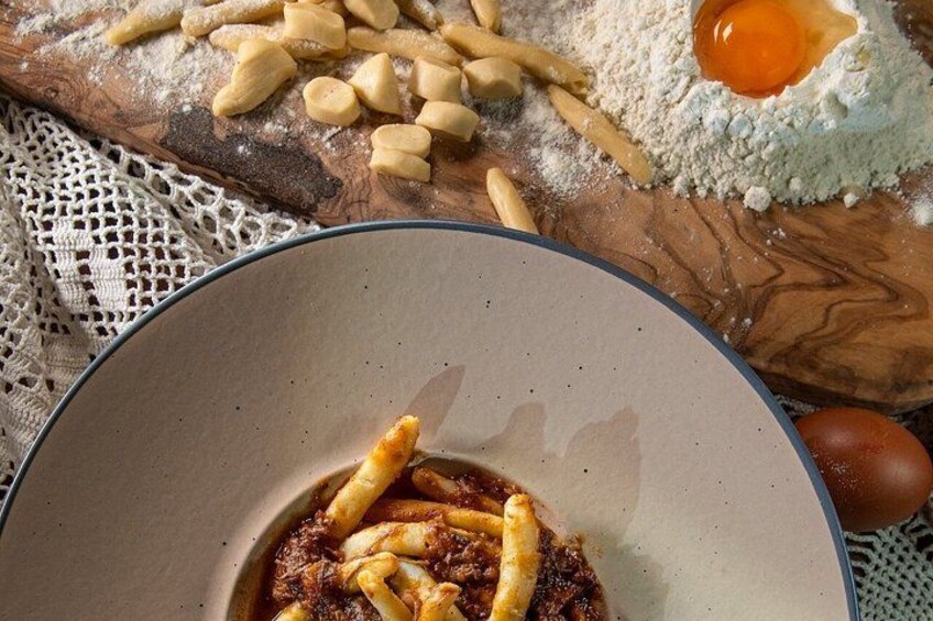 A bowl of pasta with sauce, a whole egg, and flour on a wooden surface. 4