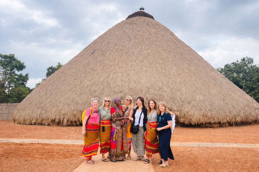 A group of people standing in front of a large thatched structure. 2