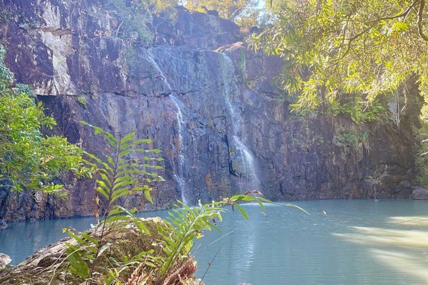 A waterfall cascading down a rocky cliff into a calm body of water, surrounded by lush greenery. 4