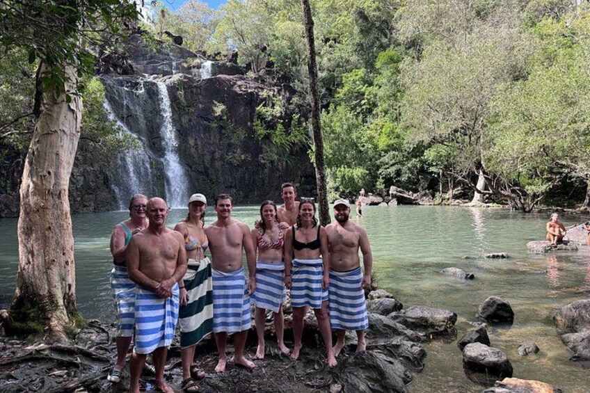 A group of people standing by a waterfall in a forested area. 1