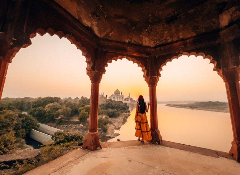 A person standing in a structure with arches, overlooking a body of water and a distant white building. 1