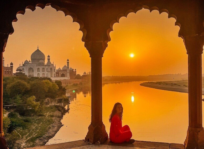 A sunset view of the Taj Mahal with a person sitting in an archway. 3