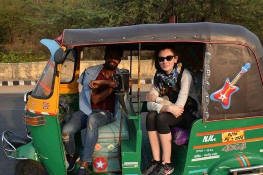A green auto-rickshaw with a man and a woman inside, a guitar decal on the side, and a star emblem on the front. 4