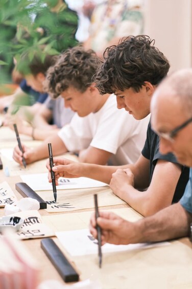 People sitting at a table, writing with pens. 4