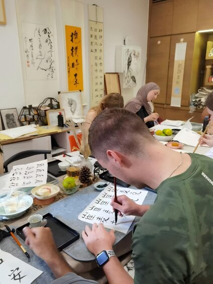 A person practicing calligraphy with a brush on paper, surrounded by calligraphy tools and artworks. 2