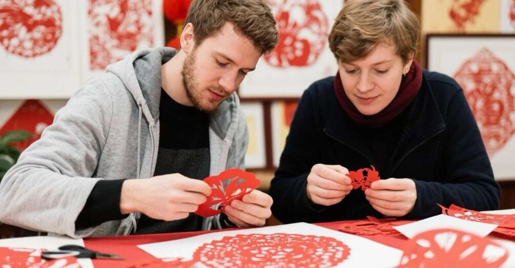 Two people crafting red paper cutouts at a table. 5