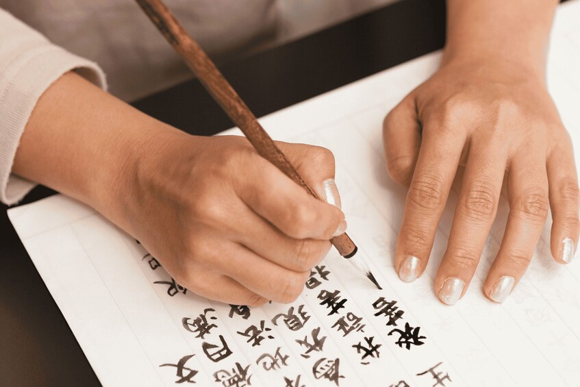 A person writing Chinese characters on paper with a brush. 3