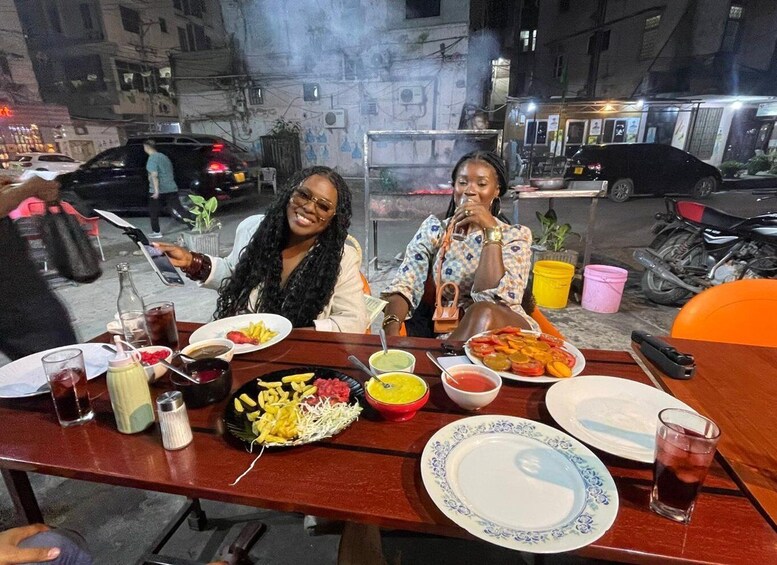 Two women dining at an outdoor table with various dishes and drinks. 3