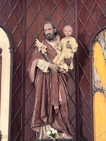 A statue of a robed figure holding a child, with a floral arrangement at the base. 2