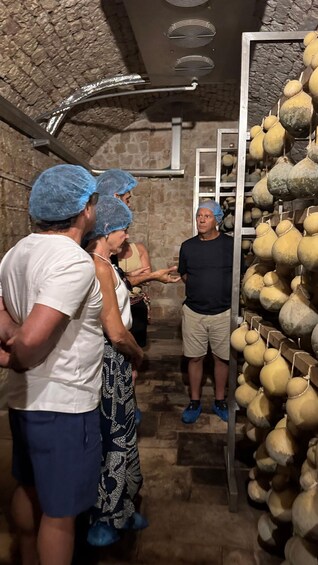 A group of people in a stone-walled room with a ventilation system and a rack of gourds. 1