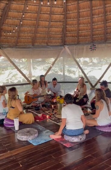 A group of people sitting on mats inside a thatched-roof structure. 4