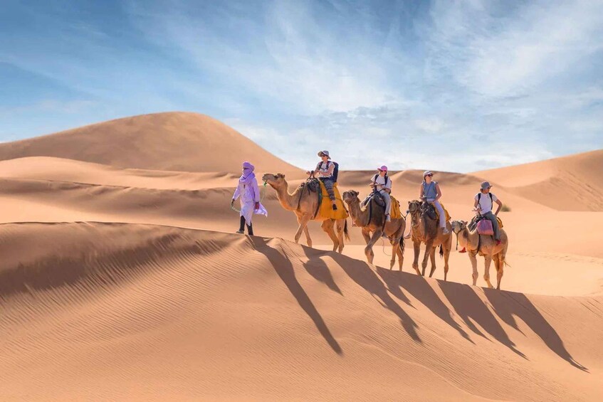 A group of people riding camels across sand dunes under a clear sky. 1
