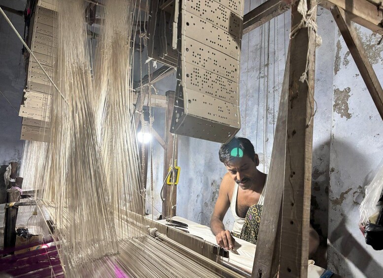 A person weaving on a loom in a workshop with wooden structures and metal components. 3