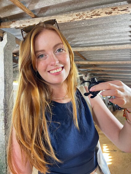 A person with long hair wearing a blue top and sunglasses, holding a small black object. 1