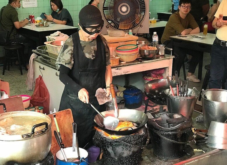 A person cooking with a wok on an open flame, surrounded by various cooking utensils and pots. 4
