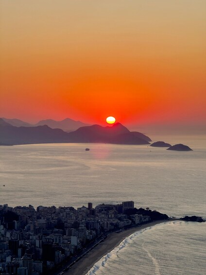 A sunset over a coastal city with buildings along the shore and mountains in the distance. 2